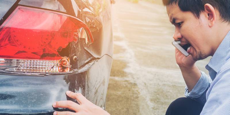 Un conducteur au téléphone constate les dégâts à l'arrière de sa voiture