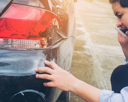 Un conducteur au téléphone examine le feu arrière endommagé de sa voiture
