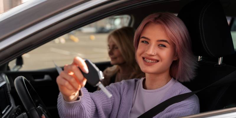 Une jeune conductrice souriante montre les clés de sa voiture depuis le siège conducteur