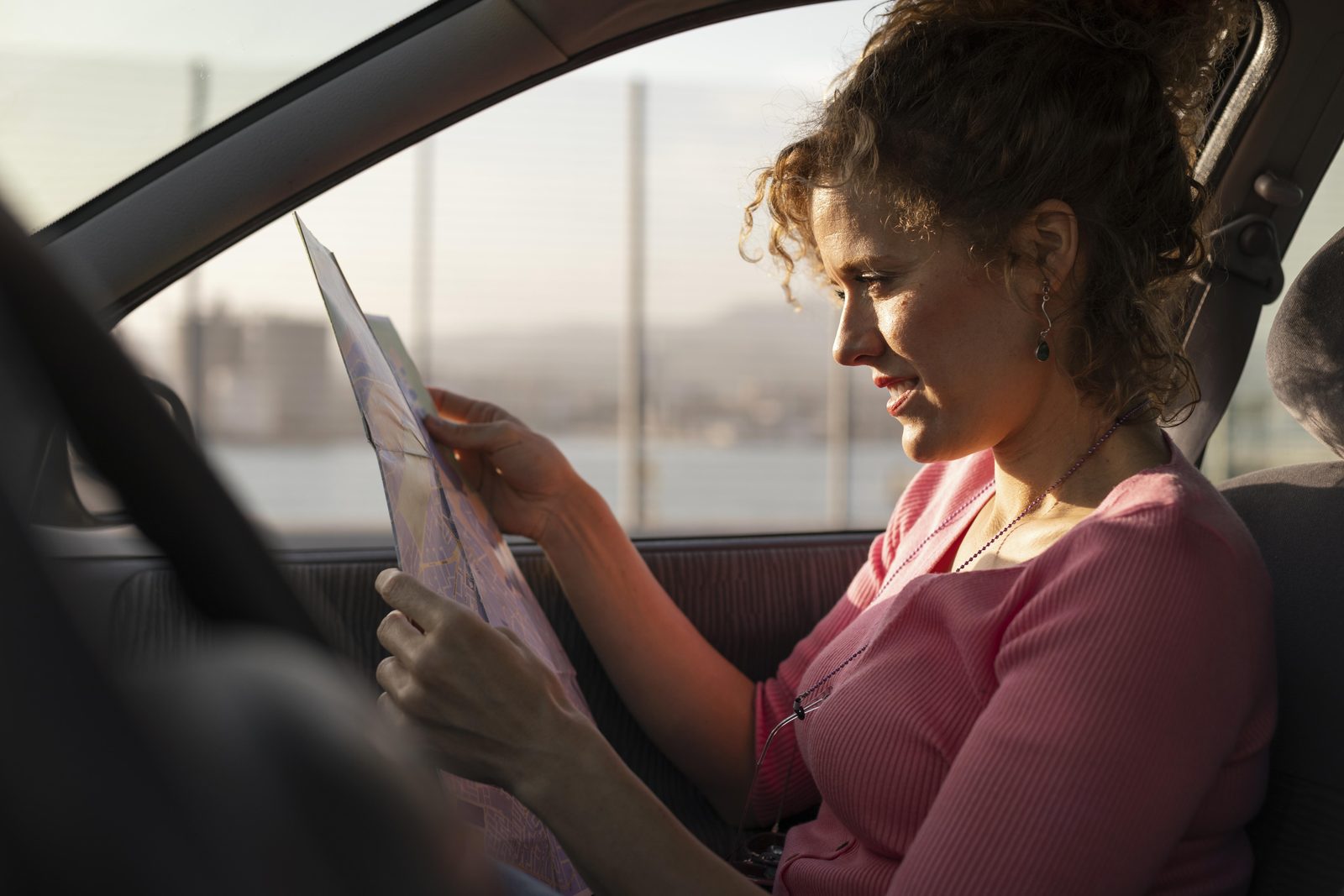 Une femme consulte une carte routière pliée, assise dans une voiture